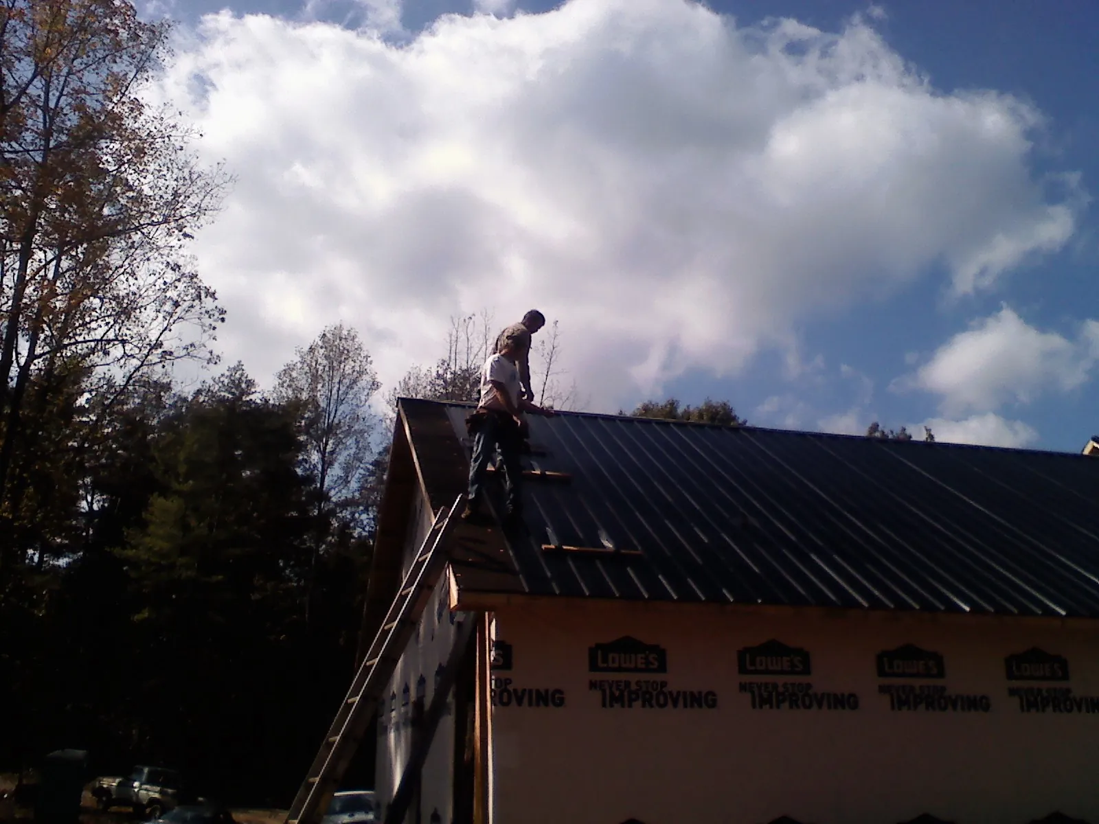 Roofer fastening dark metal panels high against a cloudy sky, from a Roof Inspection job in Forest City